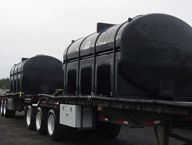 Two large black poly tanks mounted on a flatbed trailer