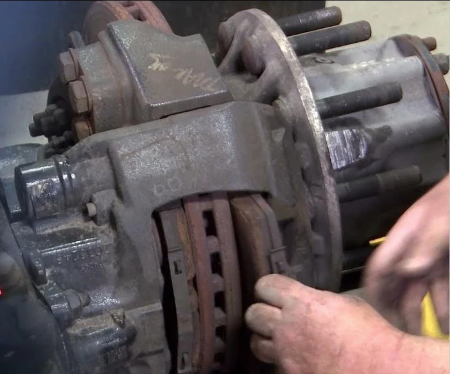 Mechanic inspecting a worn brake caliper and pads on a heavy truck axle
