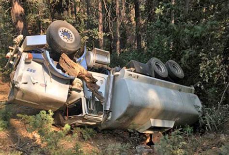 A rolled-over fire fighting water tender on a wooded roadside