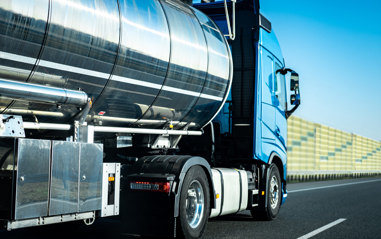 Close-up of a tanker truck's stainless steel tank and rear axles on the highway